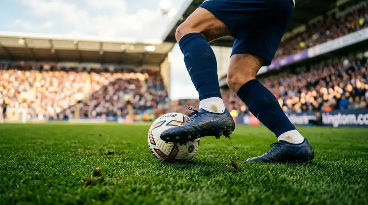 Detail nohou fotbalisty vedoucího míč na zeleném trávníku otevřeného stadionu při odpoledním zápase