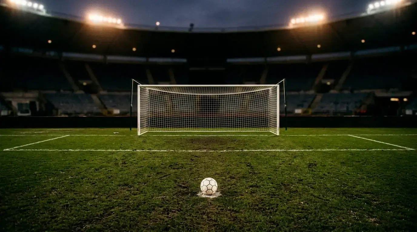 Prázdná fotbalová branka s míčem na značce pokutového kopu na osvětleném stadionu po skončení zápasu