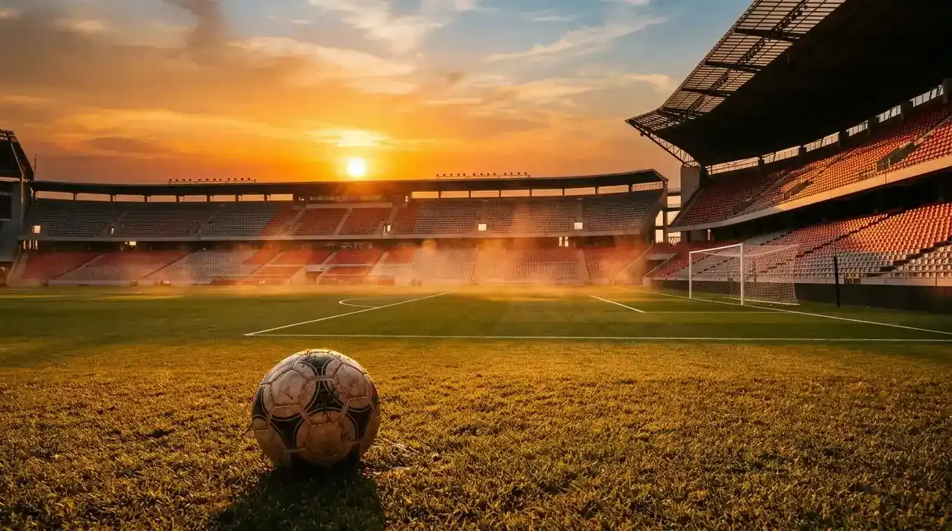 Fotbalový míč na trávníku rozpáleného stadionu při západu slunce před večerním zápasem